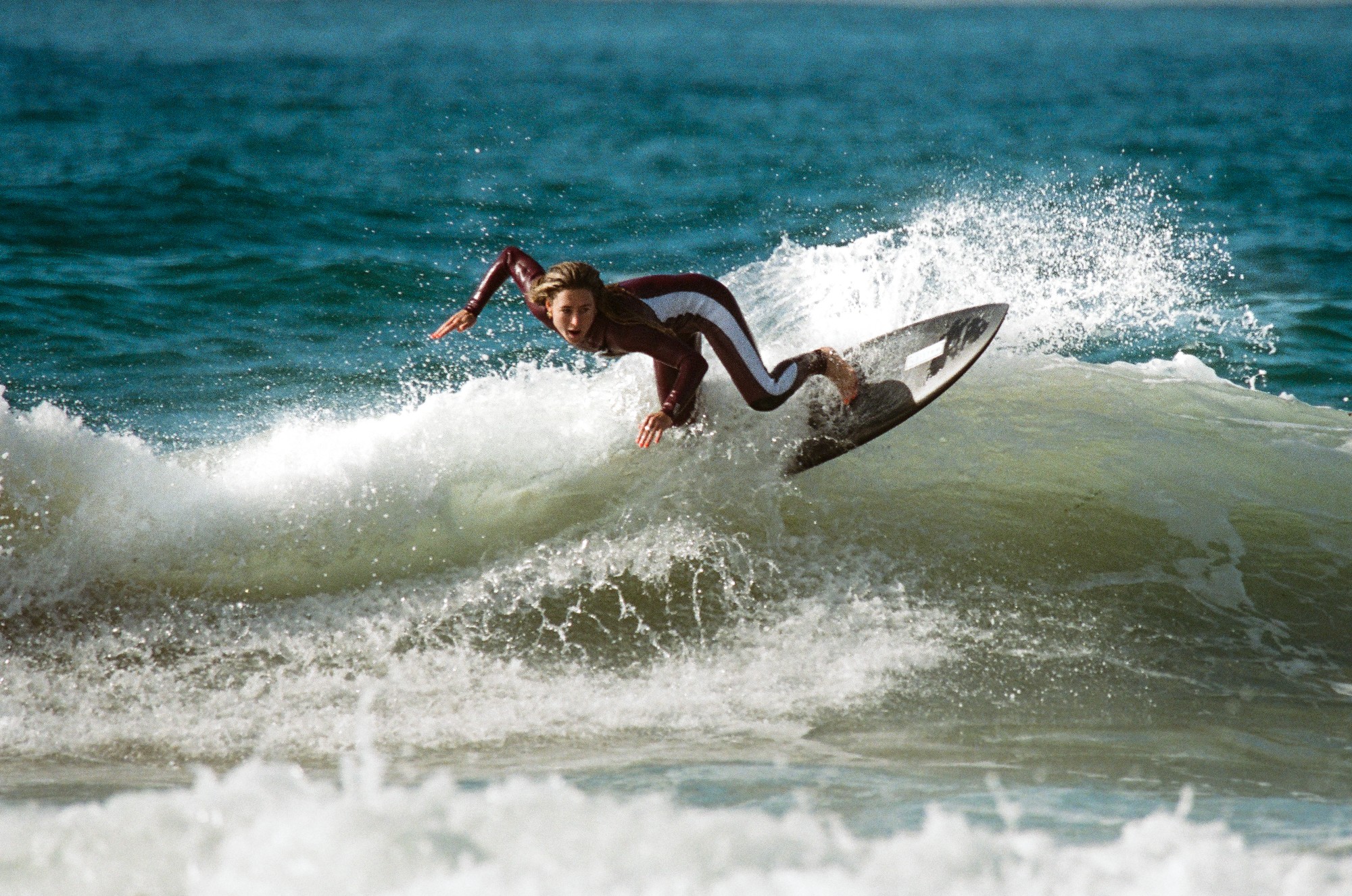 Surfer carving off the top of a green wave, throwing spray behind the board