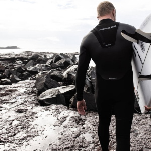 Surfer in a wetsuit pulling on a glove beside the sea