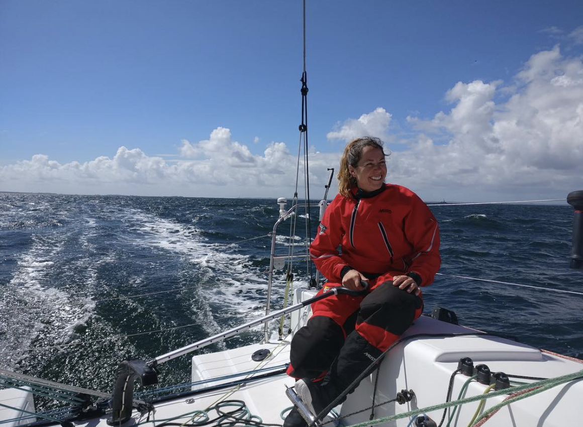 Sailor in a red waterproof jacket sitting on the stern of a yacht sailing in open water