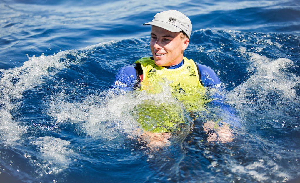 Sailor in a yellow racing bib splashing in the sea after being thrown in to celebrate