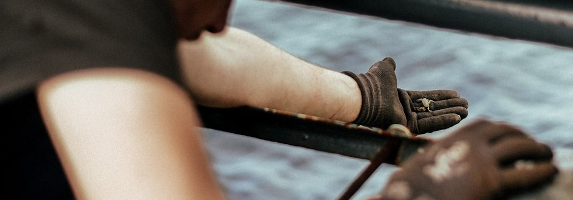 Close-up of bare arms and a worn work glove hauling a line over a boat's gunwale