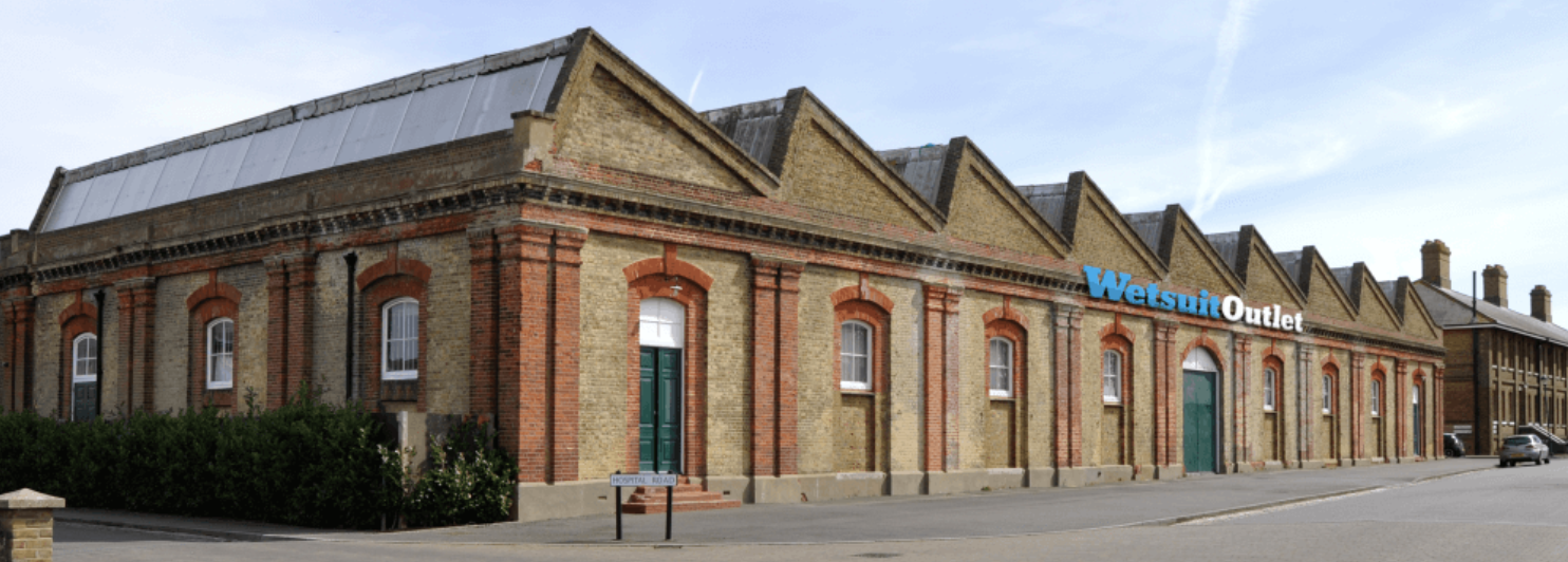 Long red-brick warehouse building with Wetsuit Outlet signage along the roofline